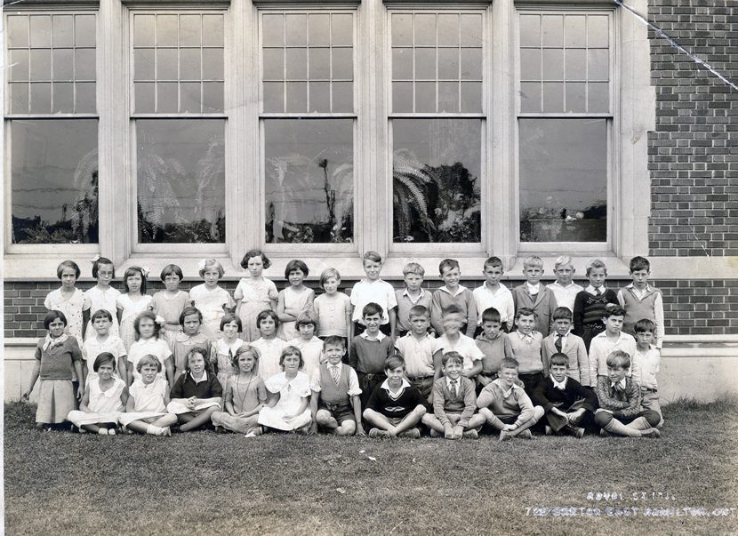 Class photo of forty-two boys and girls on the lawn under the windows of a large brick building.