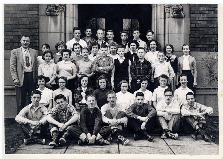 Thirty eight young men and women pose for a class photo with their male teacher circa 1940.