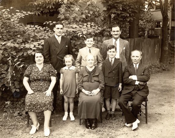 Eight members of the Balinson family sitting for a family portrait outside in a treed alley.