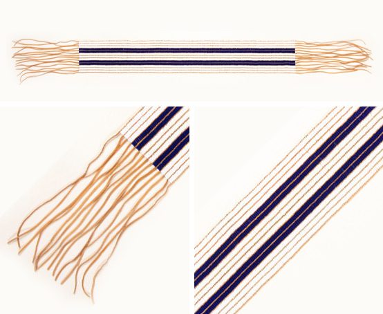 The Two Row Wampum Belt in white and purple with fringe at each end.