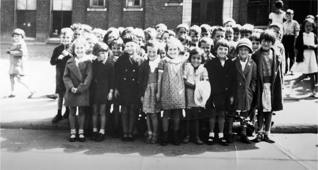 Over twenty young girls and boys stand for a group photo outside a brick building.