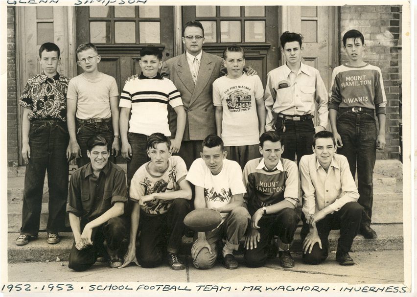 Eleven members of school football team and coach on the steps outside in front of doors.