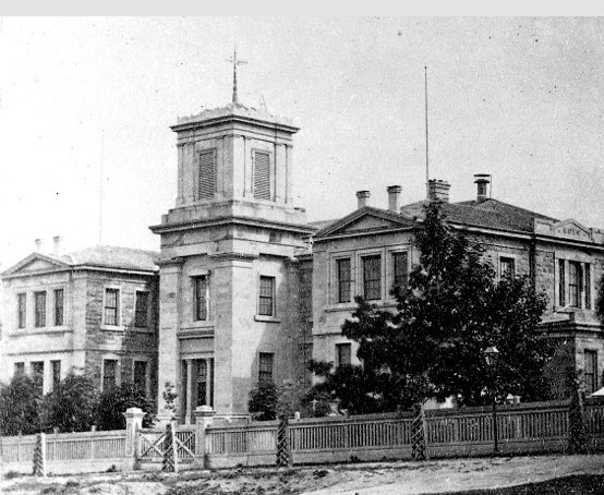Large Georgian-style building with bell tower, fenced property and mature trees.