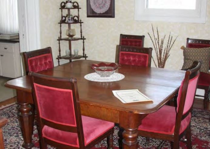 Dining room with wooden table and four wooden chairs padded in red velvet.