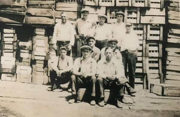 Ten Dominion Glass workers in front of stacks of wood pallets.
