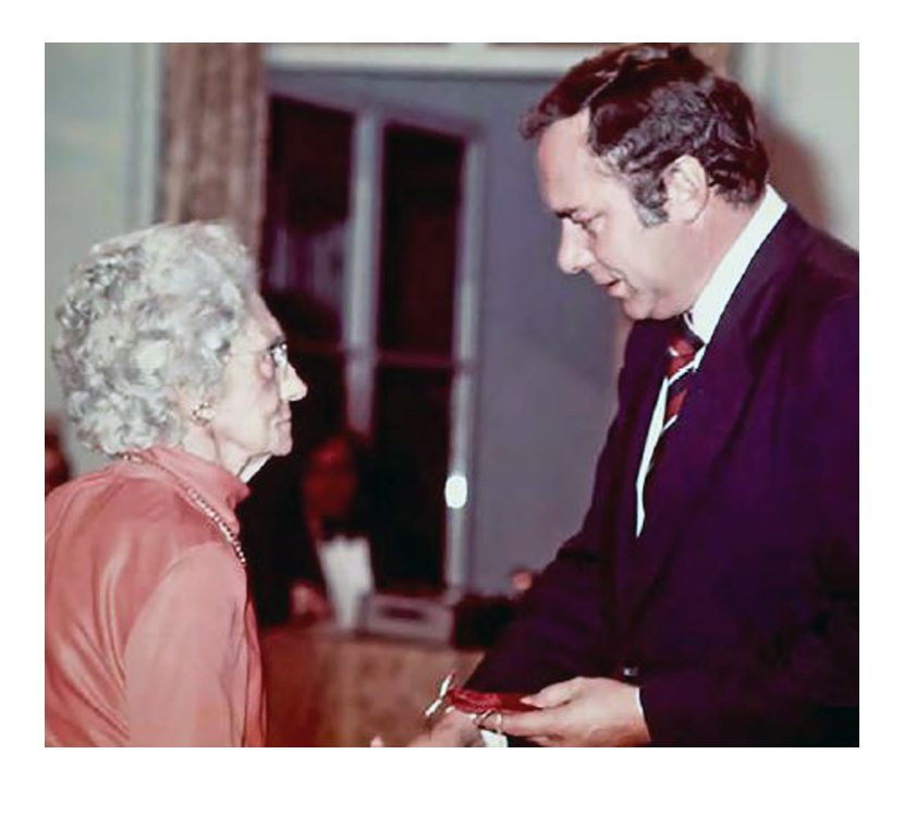 A senior woman fashionably dressed has an exchange with a younger man in a suit.
