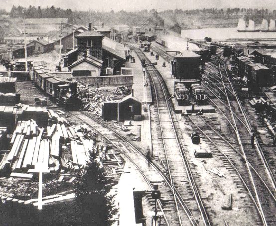 A railway yard and station showing buildings and schooners on the bay.