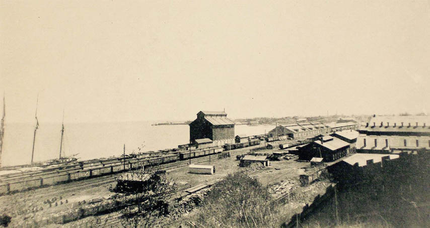 Railway yard showing various buildings and the bay in background.