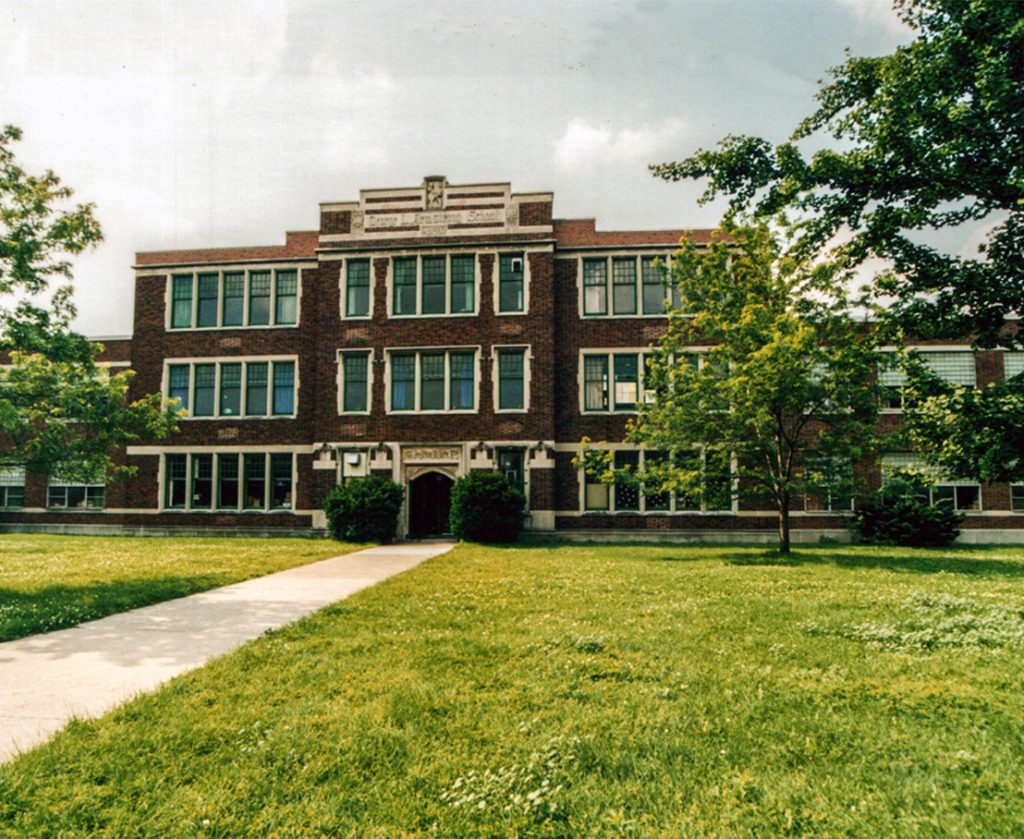 Three story brick building with expansive lawn, trees and shrubs within a mature neighbourhood.