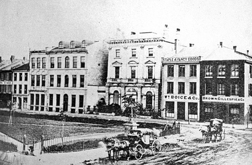 Street view of Gore Park as horses and wagons pass on dirt roads with multi story buildings in background.