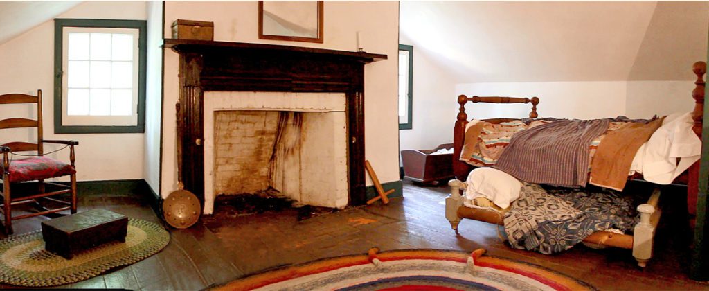 Early nineteenth century bedroom with fireplace, bed warmer, quilts and area rugs.