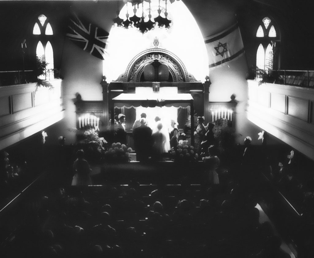 As seen from above, a wedding ceremony with onlookers takes place inside the Hunter Street Shul.