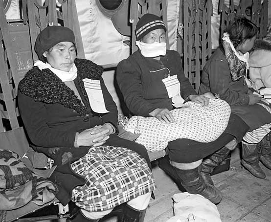 Three people wearing paper information slips pinned to their coats sitting on a bench.