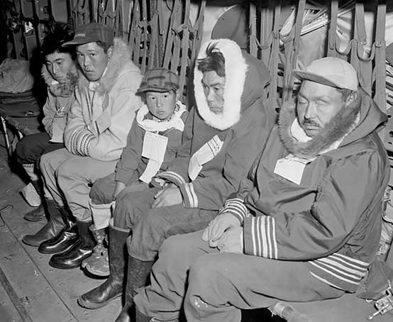 Four adults and one child wearing paper information slips pinned to their coats sitting on a bench.