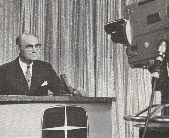 C.H.M.L. television camera zooms in on man with glasses seated at desk with a microphone.