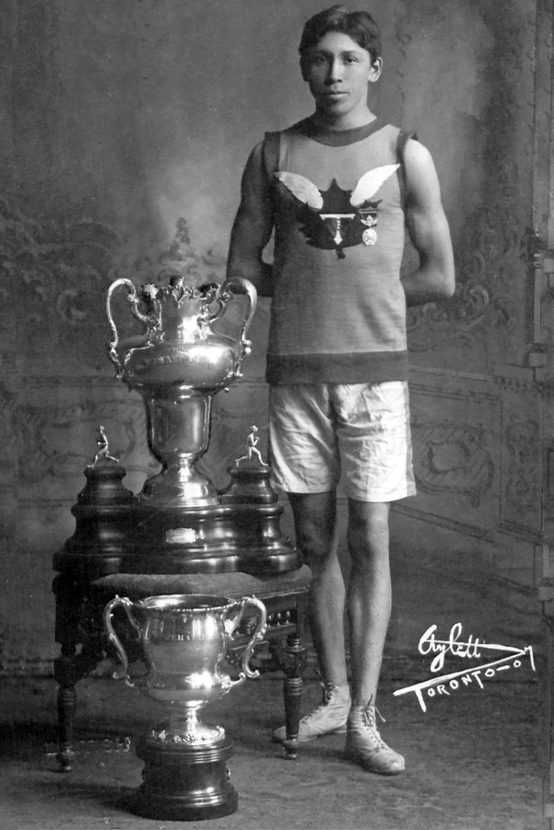 Tom Longboat standing beside two of his many trophies 1907.