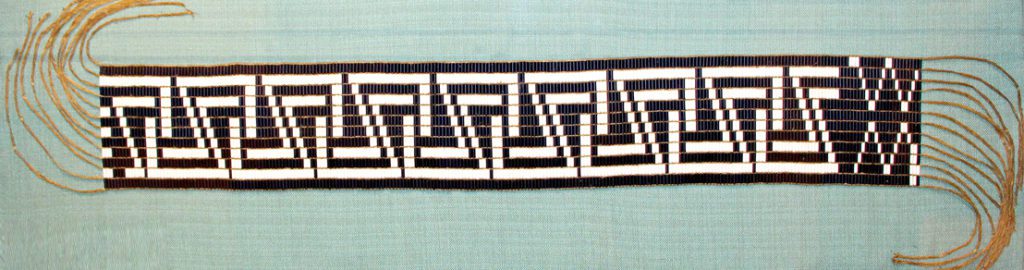 Fringed belt with white and black wampum forming a zig zag pattern.