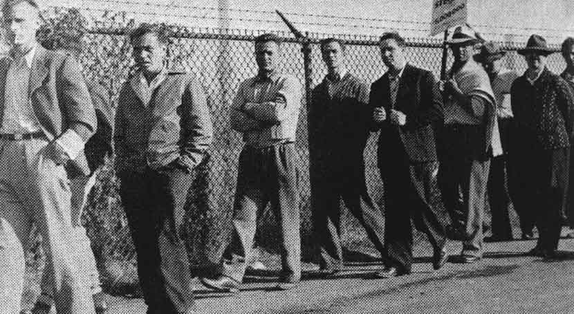 Ten men, one carrying a sign, walk the picket line.