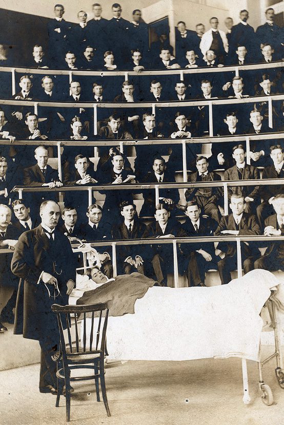 Operating theatre with fifty eight male doctors observing male doctor and patient.