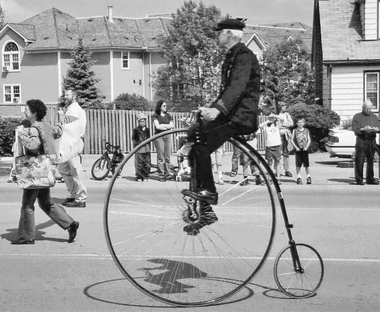 A man riding a penny-farthing direct drive bicycle in a parade.