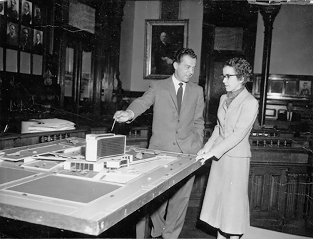 An architectural model of Hamilton City Hall sits on a table as two people converse nearby.
