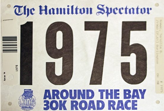 White Around the Bay Road Race runner's bib with text in blue and 1975 in black.
