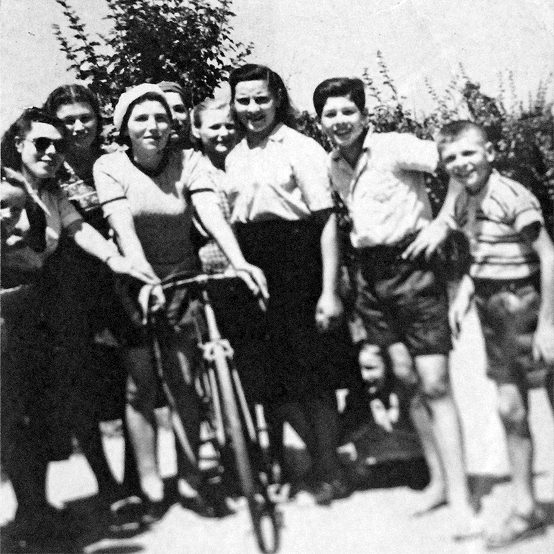 Nine people on foot and one person with a bike, pose for a photo on a warn sunny day.
