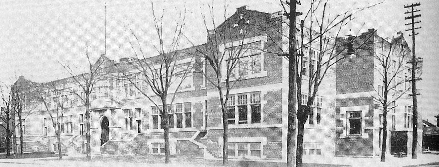Two story formal expansive brick building surrounded by mature trees.