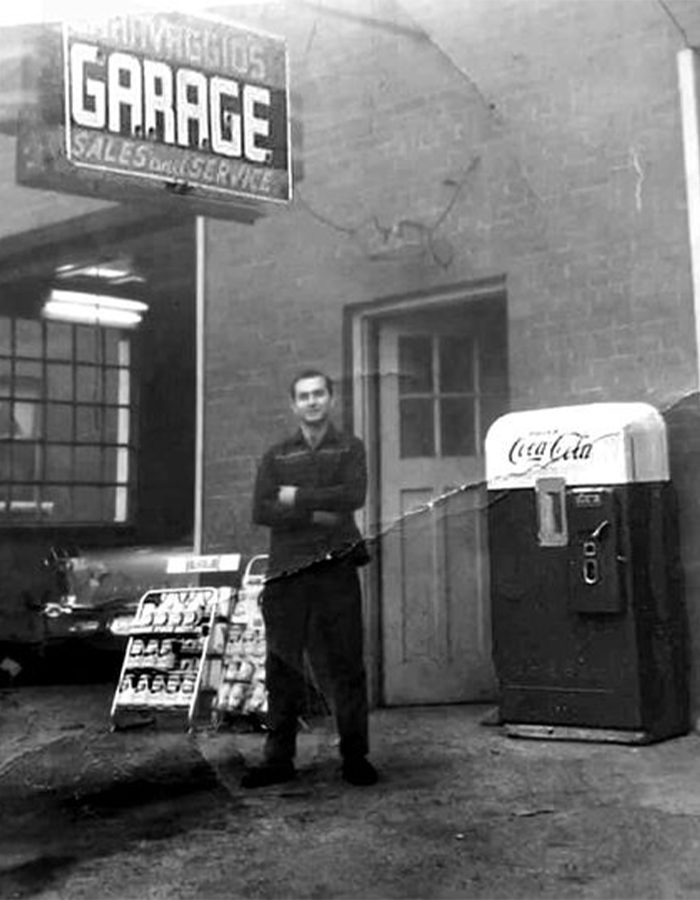 Man standing in font of garage with oil cans and Coca Cola vending machine on Gage north.