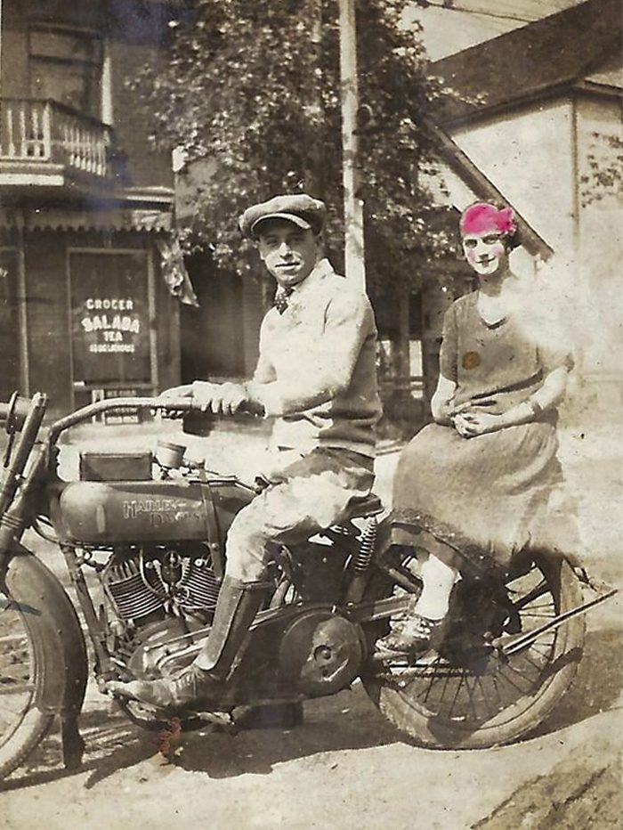 A couple sitting on a motorcycle in front of a store in 1928.