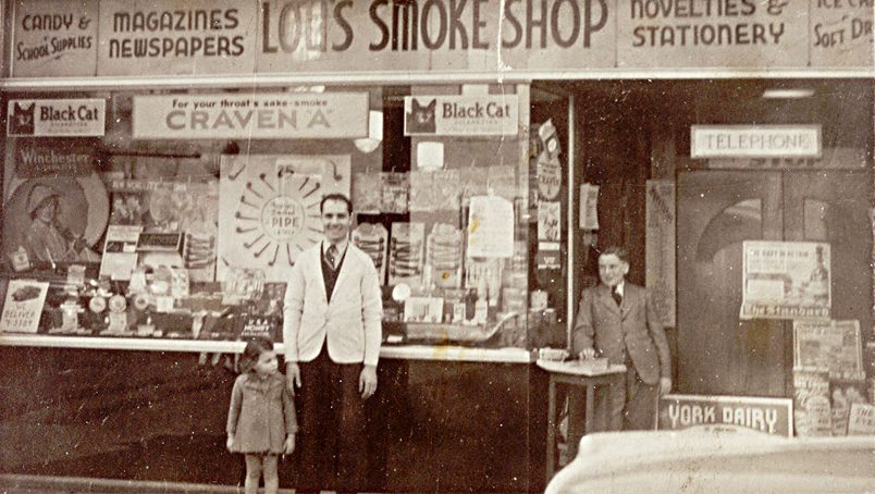 Lou's Smoke Shop storefront with adult and two children standing outside.