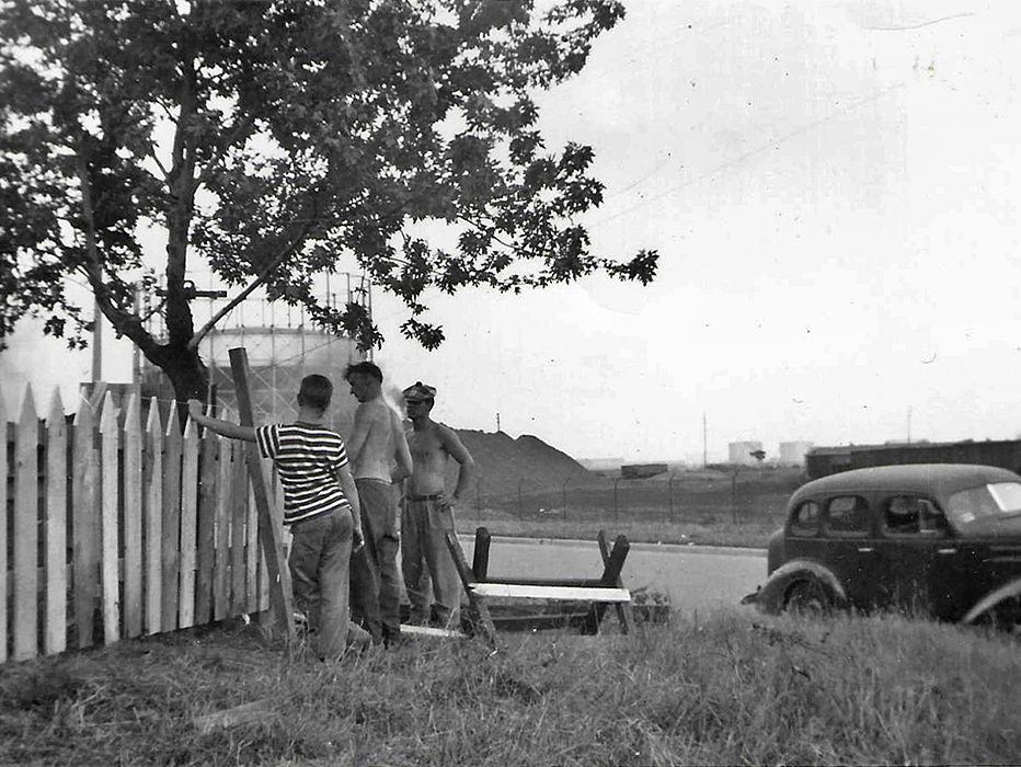 Residents repairing a fence on Plymouth Street, Gasometer and coke piles in background.