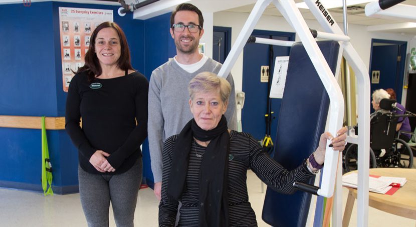 Three people stand near exercise equipment.