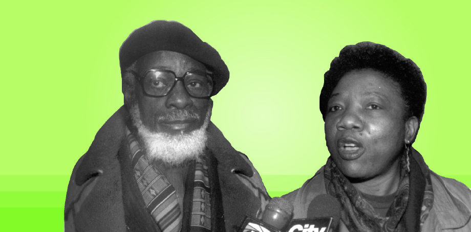 A man wearing a beret, glasses and full beard with woman speaking into media microphones.