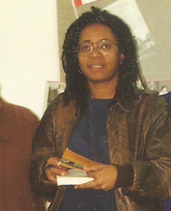 Candid picture of a young woman wearing glasses and shoulder length dreads with a book and pen.
