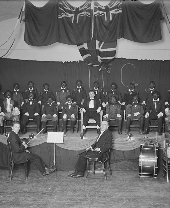 Twenty two men participating in a minstrel show with some wearing Blackface.