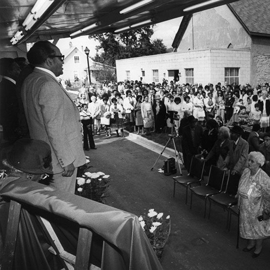 A man on a stage addresses a large crowd at an opening ceremony.
