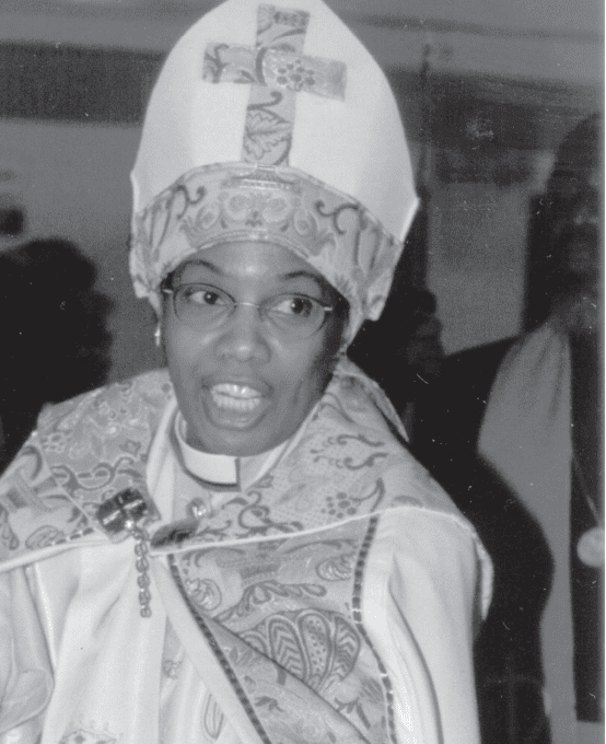 Woman with glasses wearing her Bishop's Mitre and white cassock.