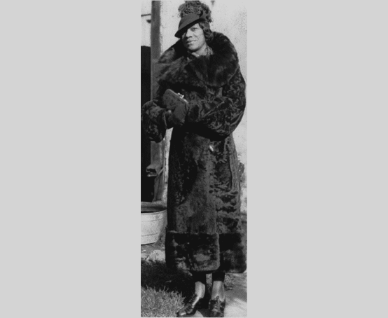 Young woman dressed in a long fur coat wearing a hat.