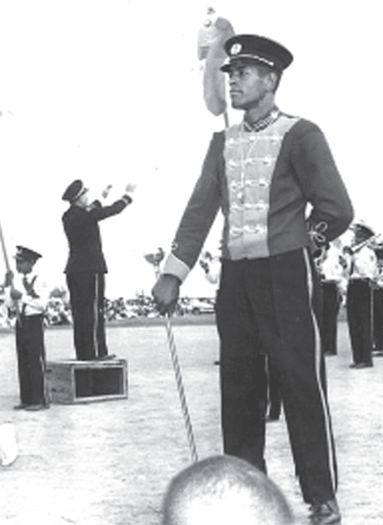 A young Drum Major stands proudly with the conductor and marching band in the background.