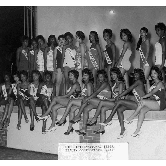 Twenty three young women wearing bathing suits, sashes and high heels pose for a group photo.