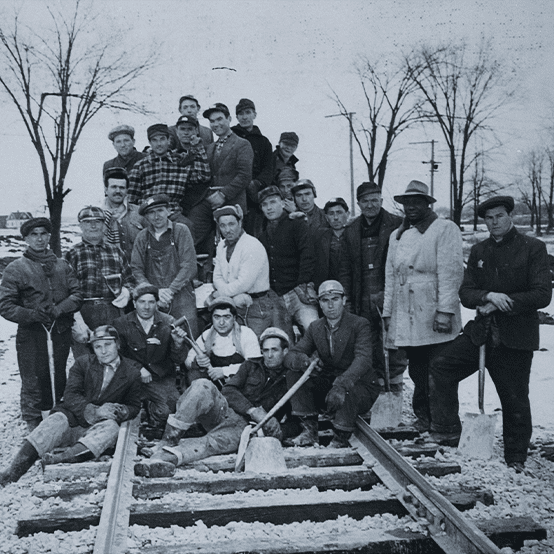 Twenty four members of a construction company pose on a set of railway tracks.
