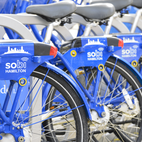 A colour photograph showing a row of Sobi Hamilton bikes. The seat and part of the rear wheel is visible, and the Sobi logo is visible above the rear wheel.