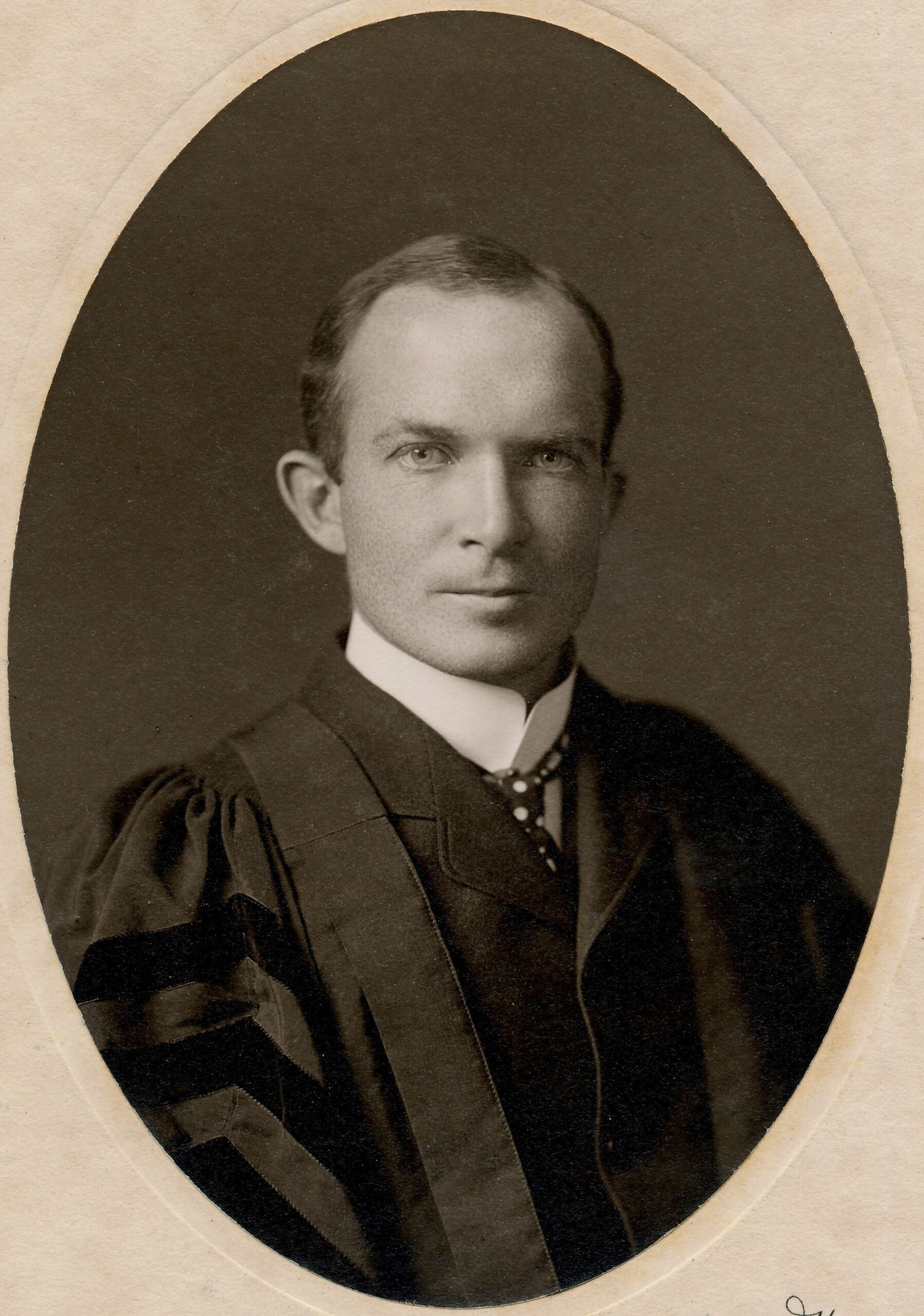 A black and white photo of a man. He is wearing black lawyers robes.