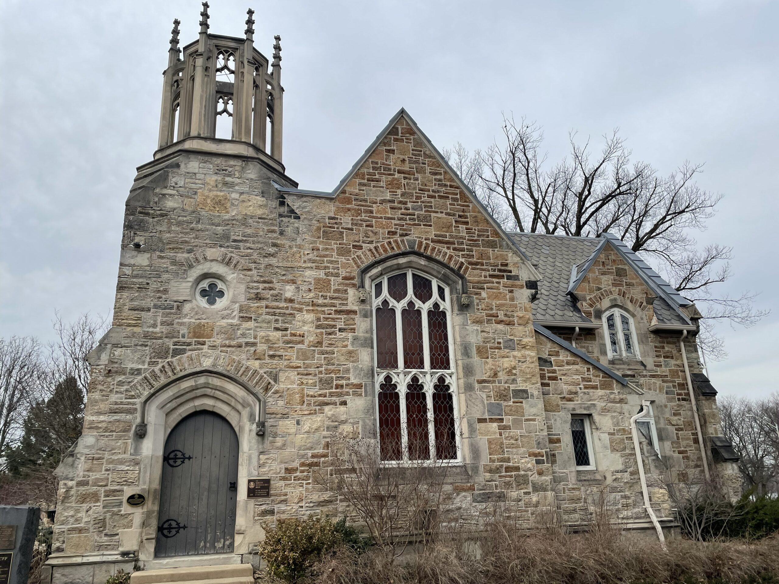 The stone Gatehouse on a grey day. The Gathouse has a bell tower and a large set of windows to resemble a chapel.