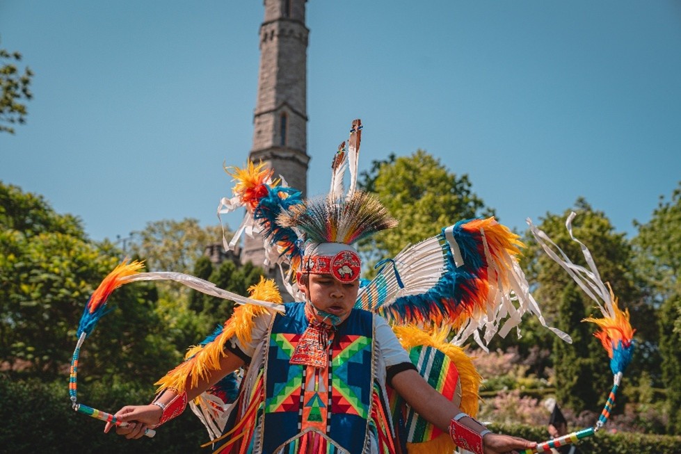 A pow-wow dancer performs in traditional regalia in front of a stone monument at the Re-enactment.