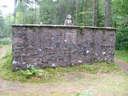 A colour photo of a stone structure that is surrounded by trees. A small stone figure sits at the top.