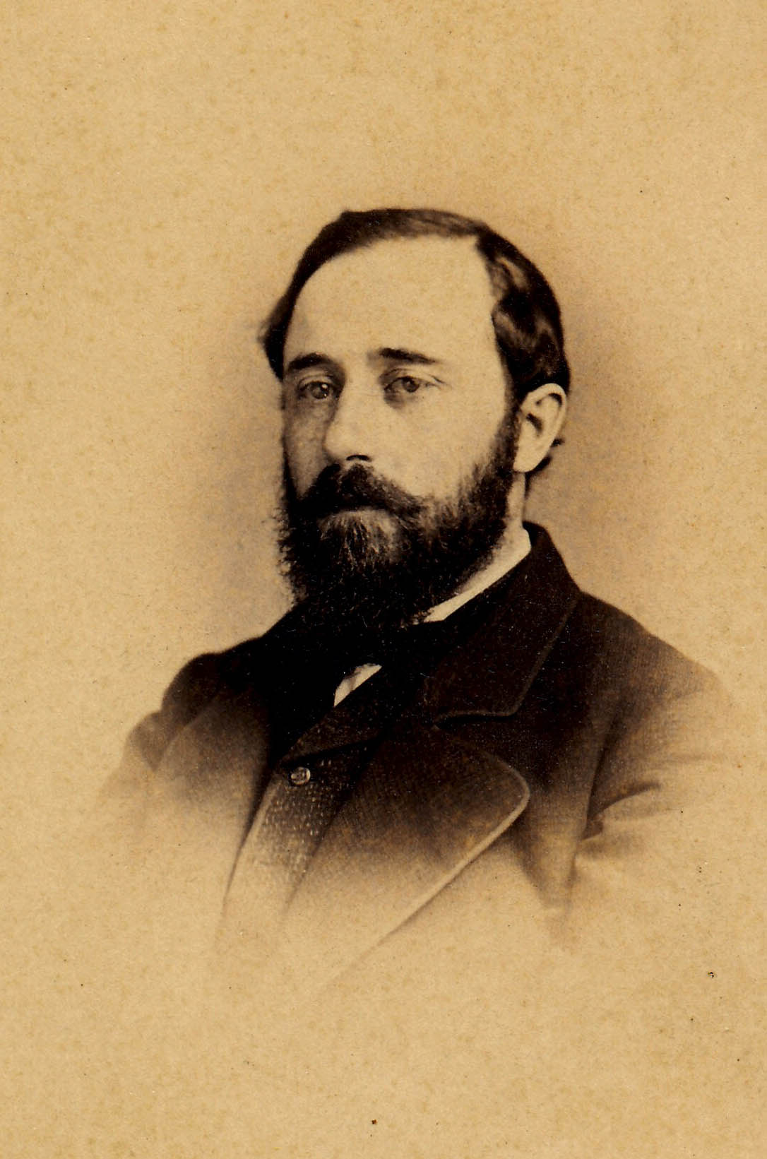 A sepia toned black and white portrait of a man looking to the left. He wears a suit and has a dark beard.