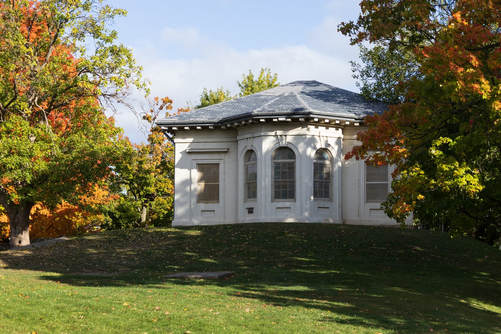 The Hamilton Military Museum, a small white building with a bay window, on a hill between trees in orange and red fall colour.
