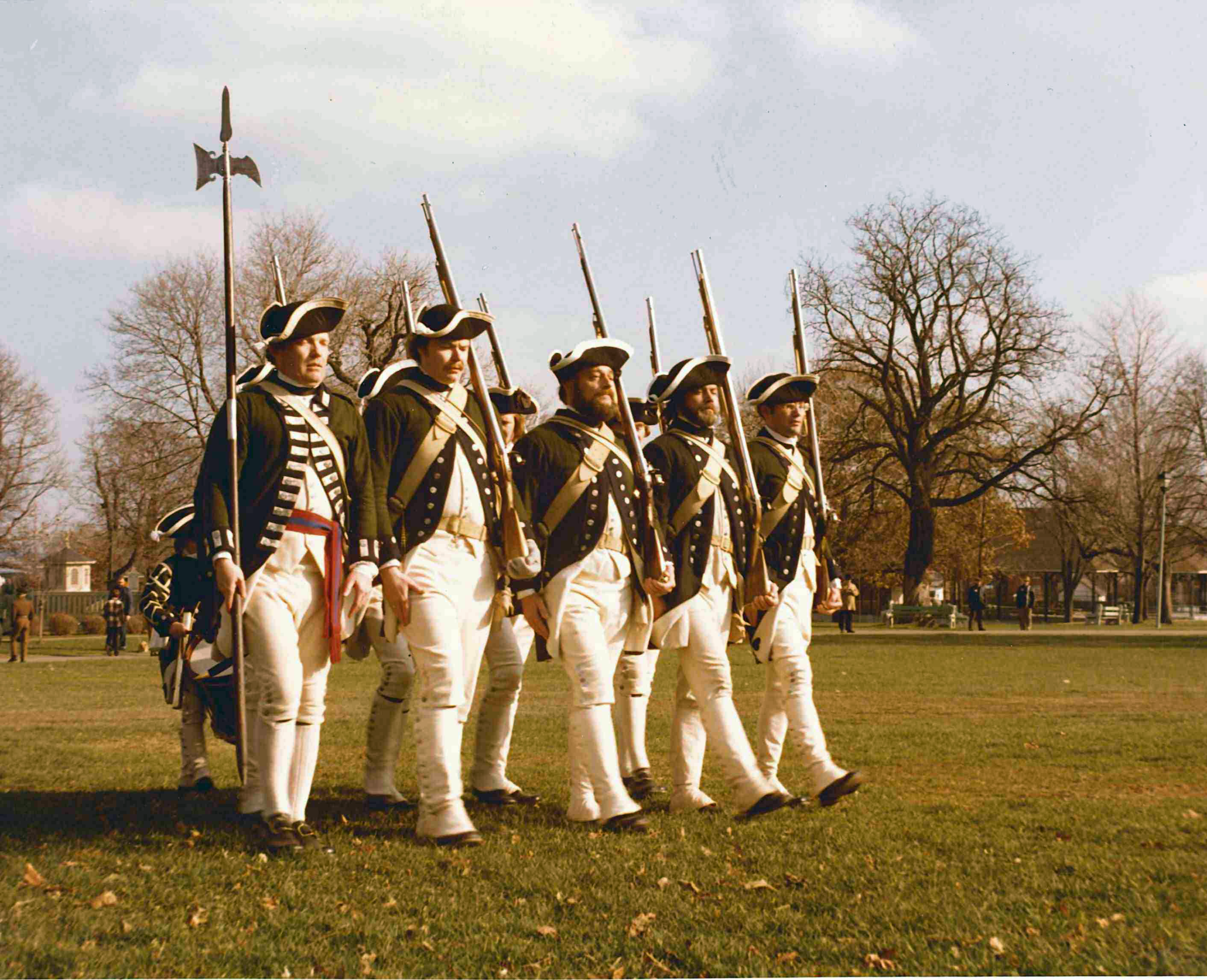 Five men wearing historic military uniforms march in a line.